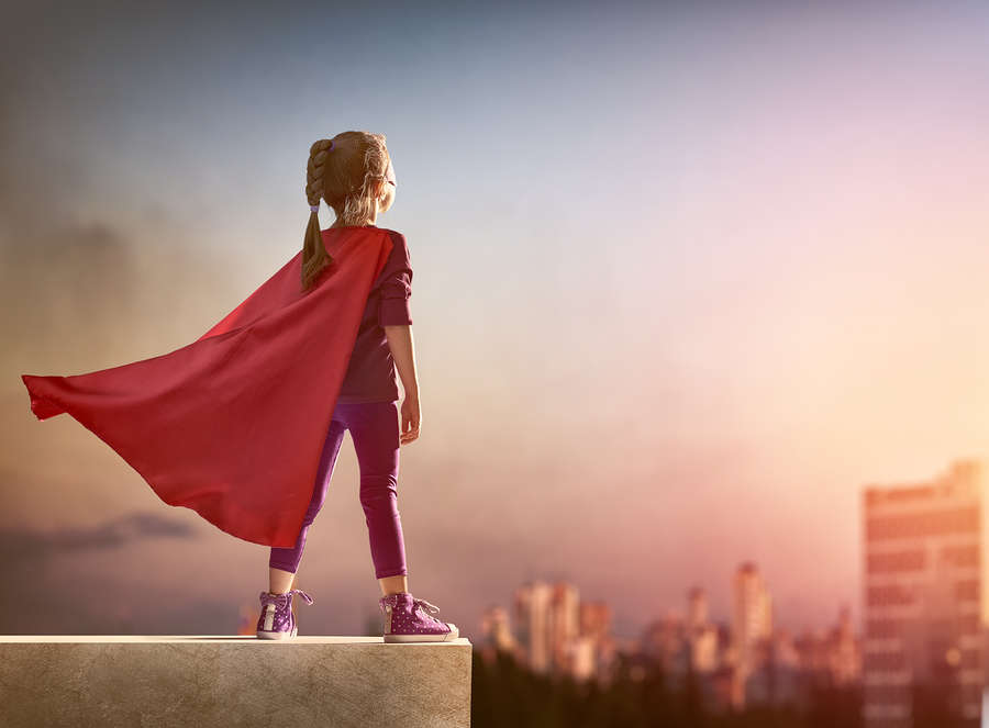 Young superhero girl wearing a cape and standing proud