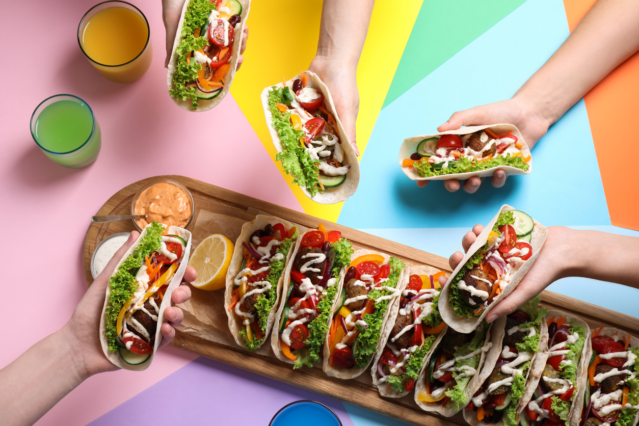 Friends holding delicious tacos on color background
